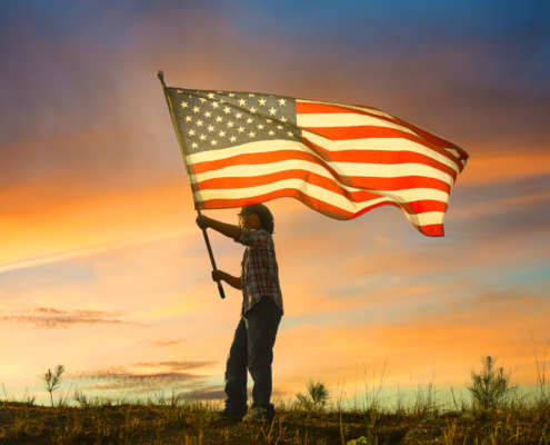 kid waving American flag at sunset
